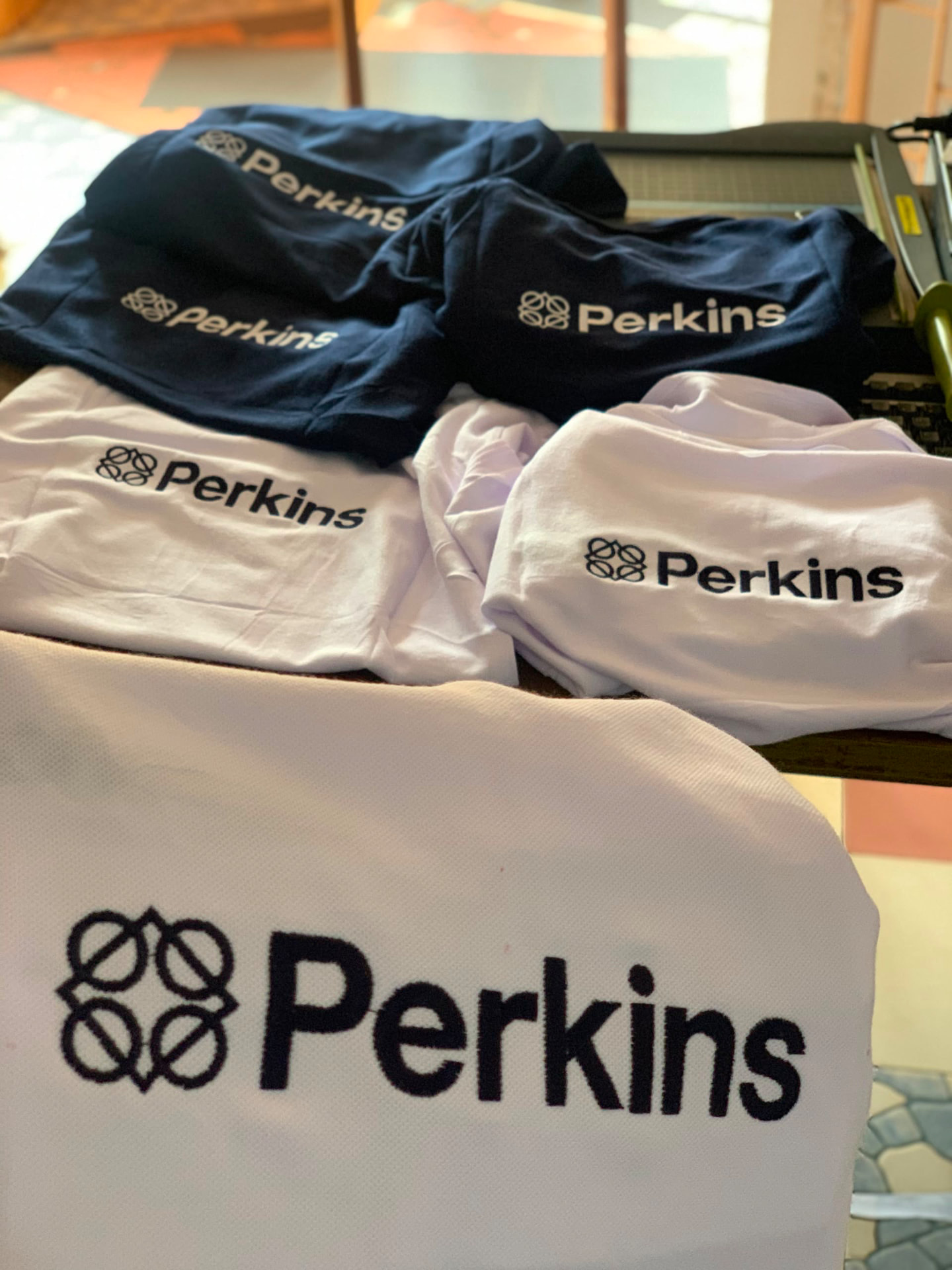 T-shirts blancs et bleus imprimés du logo Perkins par AKOYA Services à Lomé, Togo